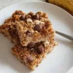 Stack of golden banana oatmeal bars with chocolate chips on white plate with scattered oats