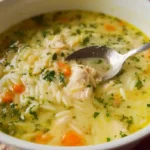 Bowl of lemon chicken orzo soup with shredded chicken, orzo pasta, carrots, and fresh herbs garnish